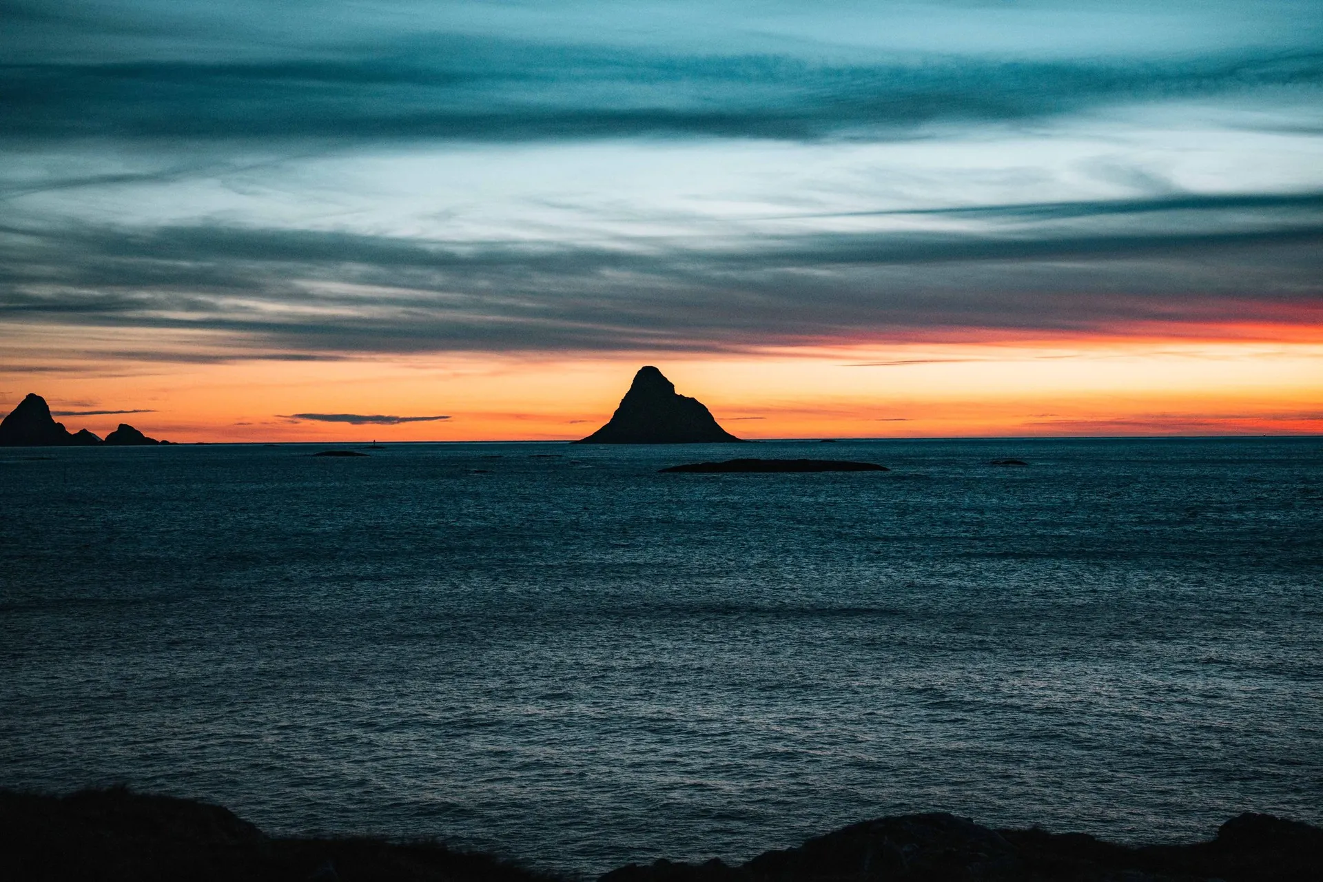 The triangular bird island of Bleiksøya as a silhouette against the orange sunset over the sea
