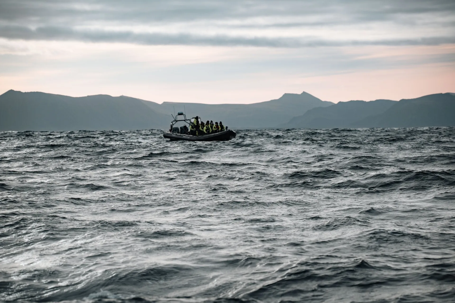 The second RIB boat full of people in neon yellow suits on the waves off Andenes, the mountains of Andøya behind
