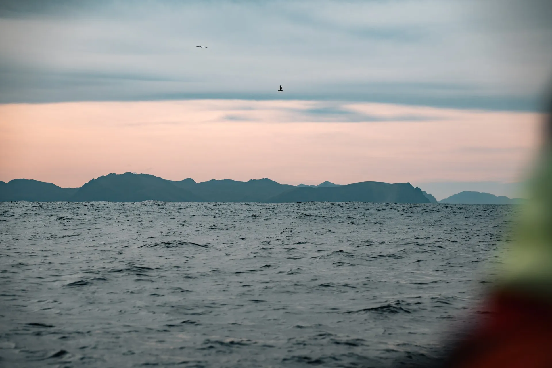 The mountains of Andøya under a pink strip of sky above the grey sea, on the way back to Andenes