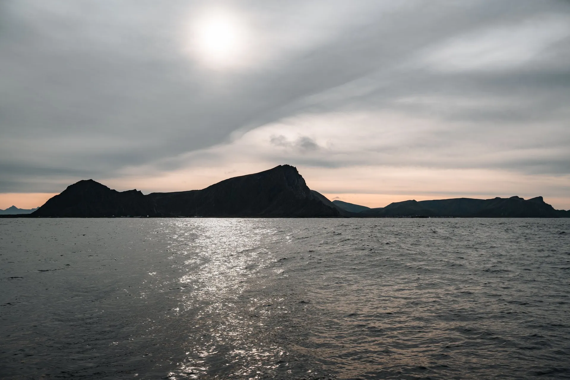 A dark island against the light, the sun glittering on the sea, on the way back to Andenes