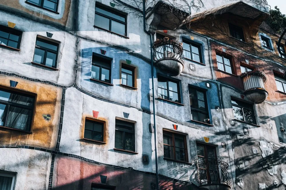 Bunte Hausfassade mit unregelmässig gesetzten Fenstern, farbigen Flächen, runden Balkonen und wellenförmigen dunklen Linien