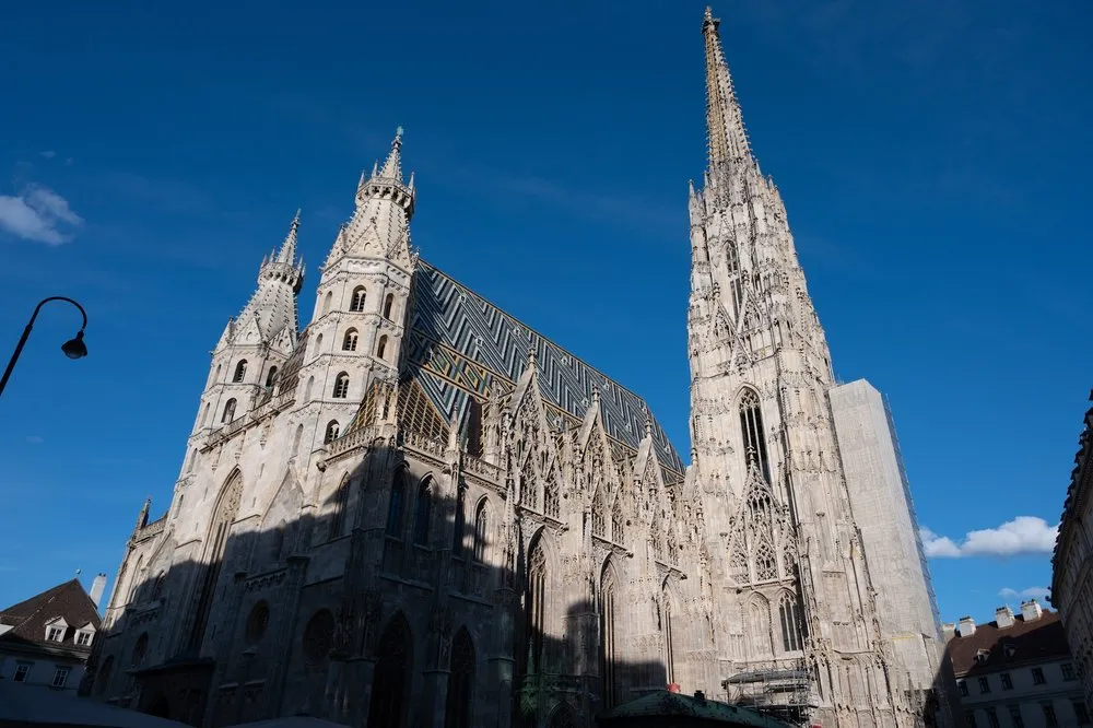 Der Stephansdom von unten gesehen, mit gemustertem Ziegeldach und hohem Turm vor tiefblauem Himmel