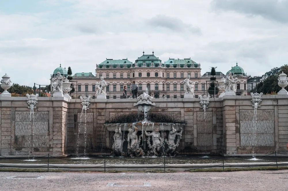 Eine Mauer mit Wasserspielen und Statuen im Garten, dahinter das Schloss Belvedere mit grünen Kuppeldächern