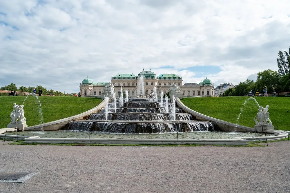 Die Wasserkaskade mit mehreren Stufen und Fontänen, links und rechts Statuen, im Hintergrund das Schloss unter bewölktem Himmel
