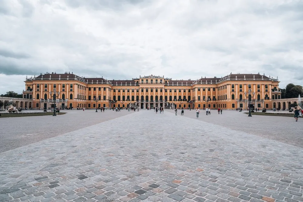 Schloss Schönbrunn in seiner ganzen Breite hinter einem grossen gepflasterten Platz unter grauem Himmel